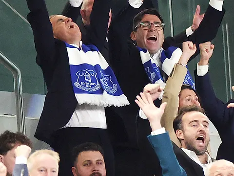 Fans in a stadium stand celebrating, some wearing club scarves